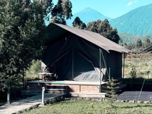 a black tent with a bed and mountains in the background at Volcanoes Over View Safaris & Camp in Nyarugina +39 photos