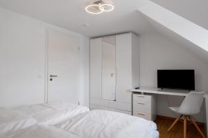 a white bedroom with a bed and a desk with a tv at Ferienwohnung Alte Münz in Müllheim