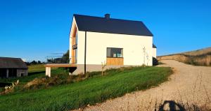 a small white house with a black roof on a road at Dom Skomackie Wzgórze widok na jezioro in Skomack Wielki