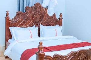a bed with a wooden headboard and white sheets and pillows at Innos Royale Suites in Rukungiri
