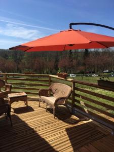 a wooden deck with a red umbrella and two chairs at Gîte Le clos du bannet in Givonne