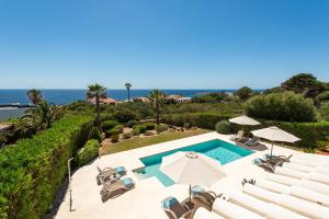 a swimming pool with chairs and umbrellas and the ocean at Villa Mariposa in Sant Lluis