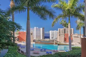 a swimming pool with palm trees and buildings at Bugalú Playa Paraíso in Adeje