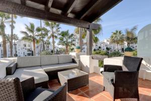 a patio with a couch and chairs and palm trees at Frontline paradise townhouse in Estepona