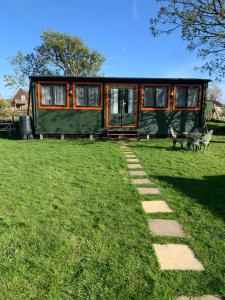 a green tiny house in a field with a pathway at Modern Cabin with large private garden in Old Romney