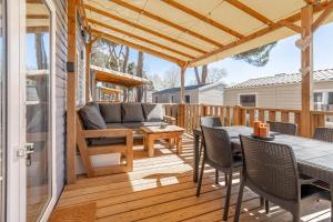 a patio with a couch and tables on a deck at Mh sympa au camping domaine la yole in Vendres