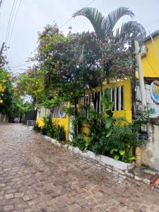 a yellow building with trees and plants next to a street at Roses hostel e pousada in Pipa