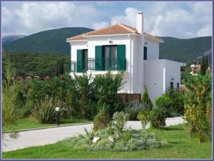 a white house with green windows and a road at Sami Beach Villas Nefeli in Karavomylos
