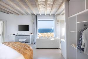a white bedroom with a view of the ocean at Alegria Mykonos 7 Suites in Kalafatis