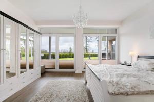 a white bedroom with a large bed and a chandelier at Haus Eiderblick in Horst