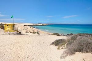 a beach with a yellow lifeguard house and people on the beach at Falco 2 in La Oliva