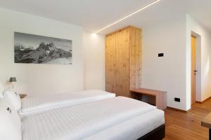 a white bedroom with a bed and a wooden cabinet at Apt Lara Ruveda 2 in Ortisei