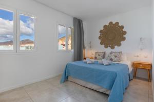 a white bedroom with a blue bed and windows at La Casa de las Hesperides in Morro del Jable