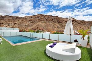 a patio with a pool and an umbrella and grass at Villa Tauro 31 in Mogán