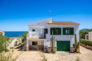 a white house with a green garage and the ocean at Ran de Mar in Son Serra de Marina