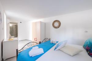 a white bedroom with a blue bed and a bathroom at Elenya Garden Retreat in Torre Lapillo