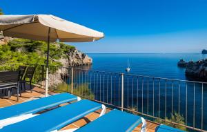 a balcony with blue chairs and an umbrella and the ocean at Cala Deia in Deia