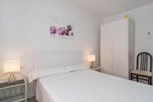 a white bedroom with a white bed and a chair at Anglesos in Can Picafort