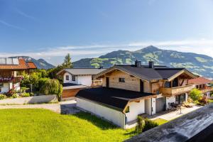 a house with a black roof with mountains in the background at Pension Heidelberg in Hopfgarten im Brixental