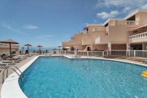 a pool with chairs and umbrellas in front of a hotel at Seaview las Americas in Adeje