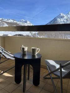 a table with two cups and a chair on a balcony at Résidence l'olympia in Montgenèvre