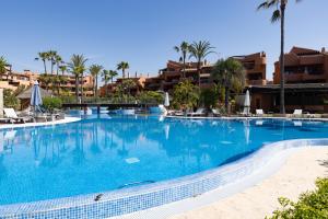 a large swimming pool with palm trees and buildings at Exclusive frontline beach penthouse in Estepona