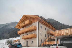 a building with wooden balconies and cars parked in the snow at Planerhof Apartment Alpenrose in Funes