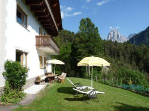 a patio with two chairs and an umbrella on the grass at Cësa Gravina Jubas in Ortisei