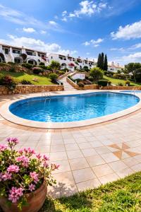 a large swimming pool in a courtyard with flowers at Costa Arenal - Biniplaya in Arenal d'en Castell