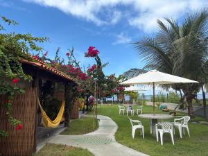 a patio with tables and chairs and an umbrella at Rancho Capilé Suítes à Beira Mar in Japaratinga