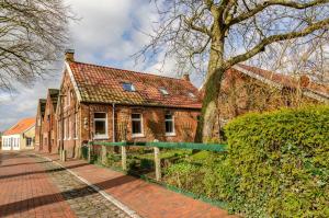 an old brick house with a tree and a fence at Gulfhof Oldersum Dachgeschoss in Moormerland