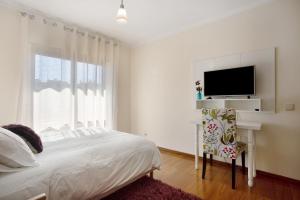 a white bedroom with a bed and a flat screen tv at T0 Grota in Buarcos