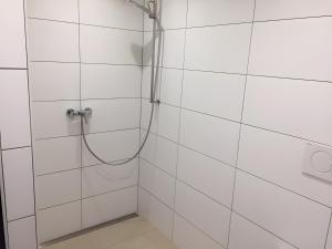 a shower with a hose in a white tiled bathroom at Ferienwohnung Schwahn in Kleinschönach +16 photos