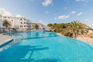 a large swimming pool with palm trees and buildings at White Sands 3.07 in Arenal d'en Castell
