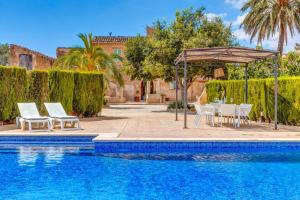 a swimming pool with chairs and an umbrella next to a house at Finca Buniferri in Llucmajor