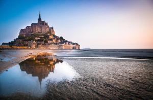 an island on the beach with its reflection in the water at Maison proche Mont St Michel in Pontorson