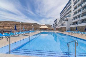 a large swimming pool with chairs and a building at Stunning Sunset Ocean View Apt in Taurito