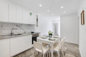 a kitchen with white cabinets and a white table and chairs at Amazing Oura Beach Apartment in Albufeira