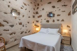 a bedroom with a white bed and a stone wall at Finca El Tablero in Tinajo