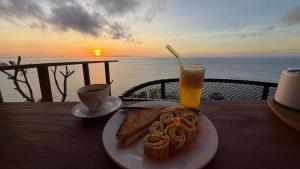 a table with a plate of food and a glass of orange juice at The Indah Cliff Sea View in Polilit