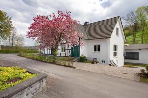 a white house with a tree with pink flowers at Gut Vasbach Ferienwohnungen in Kirchhundem