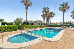 a swimming pool with palm trees and a house at Sa Calma House in Cala en Bosc