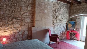 a bedroom with a stone wall with a bed and a chair at Chambre Hirondelle in L'Ile-Bouchard