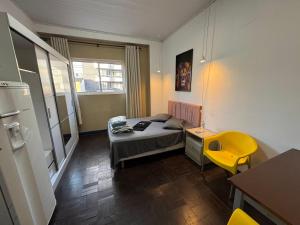 a small room with a bed and a yellow chair at Pousada Solar de Mayo in Curitiba
