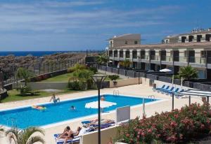 a swimming pool with people sitting in chairs next to a building at Villa in Amarilla Golf in San Miguel de Abona