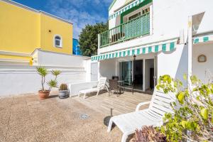a patio with white chairs and a yellow and white house at Pomelo vacacional in Arguineguín