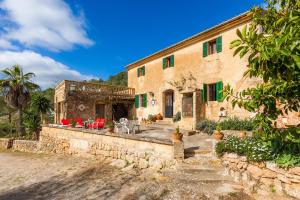a stone house with green shutters and red chairs at Finca Ses Coves in Petra