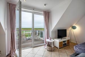 a living room with a television and a balcony at Haushälfte Süderhafen in Nordstrand