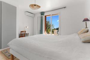 a white bedroom with a large bed and a window at Rez de villa avec jardin vue mer in Fréjus