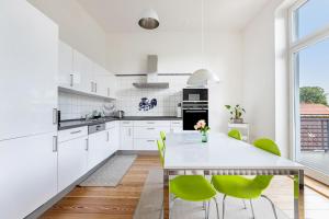 a white kitchen with a dining table and green chairs at Villa Elysium in Heide